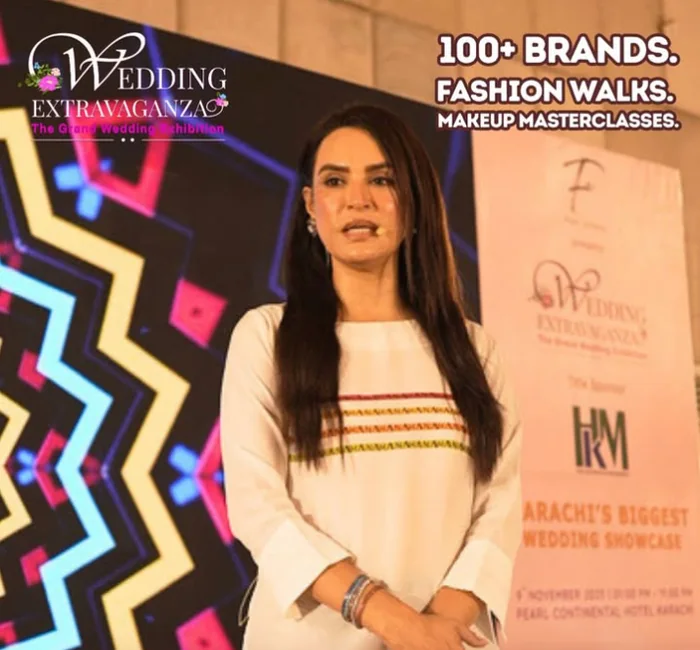 A host on stage at Wedding Extravaganza in front of the event backdrop